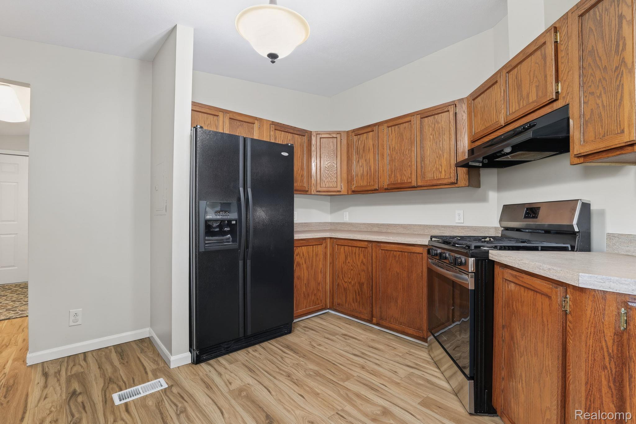 4050 West Thompson Road Linden, MI 48451 - Photo 16 of 36 Kitchen with stainless steel range with gas stovetop, black fridge with ice dispenser, light countertops, wood finish cabinetry, and light wood finished floors