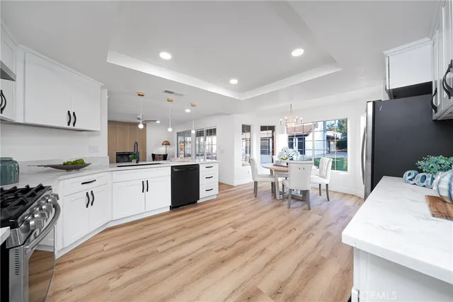 a kitchen with stainless steel appliances kitchen island granite countertop a refrigerator oven a sink dishwasher and white cabinets with wooden floor