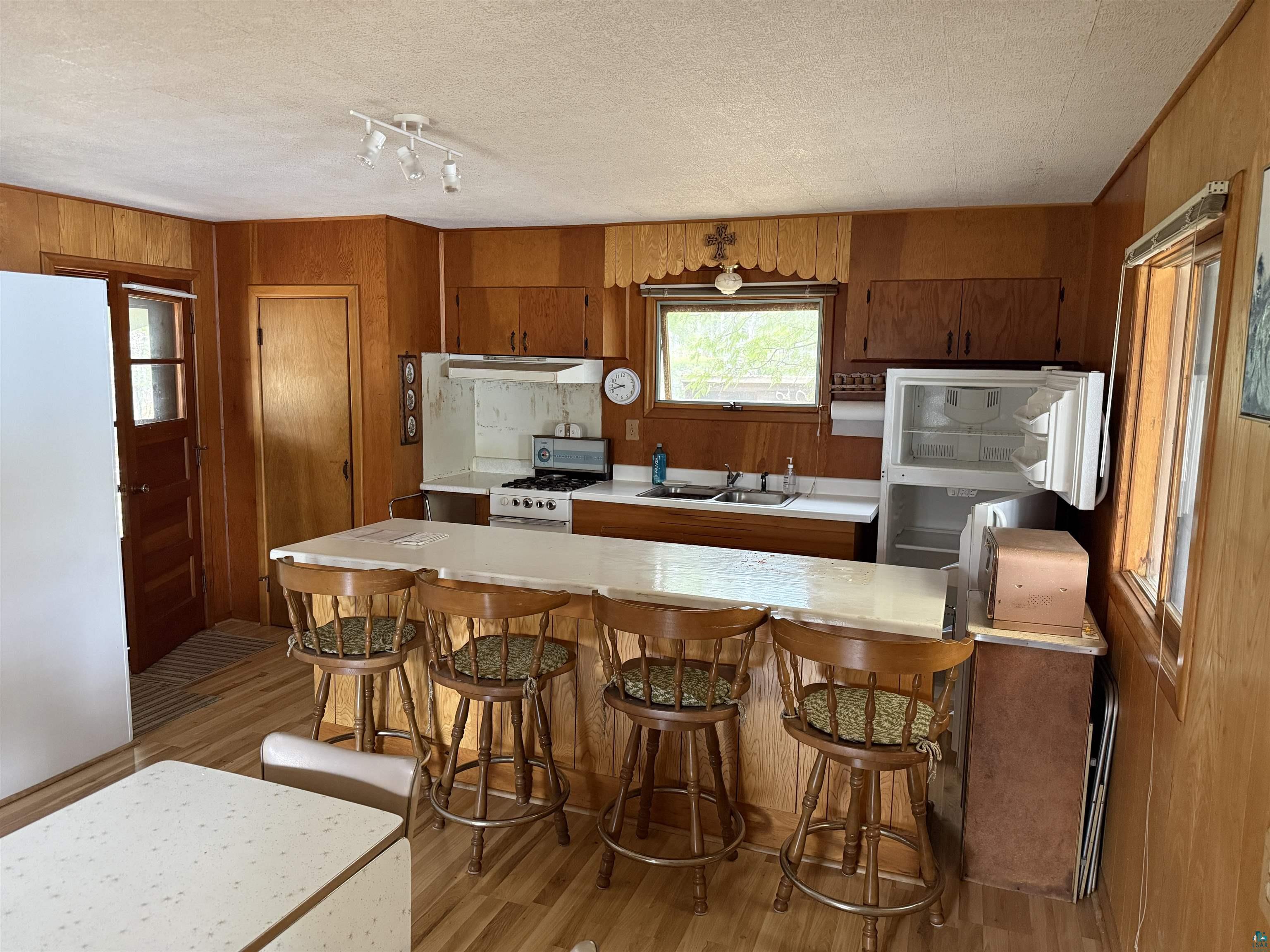 1342 Walsh Road Ely, MN 55731 - Photo 15 of 20 Kitchen featuring wood-paneled walls, a breakfast bar with seating, wood-finish flooring, propane cook stove, white countertops, and a double basin sink.