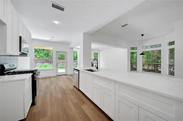 a large white kitchen with granite countertop a stove a sink a refrigerator and white cabinets with wooden floor