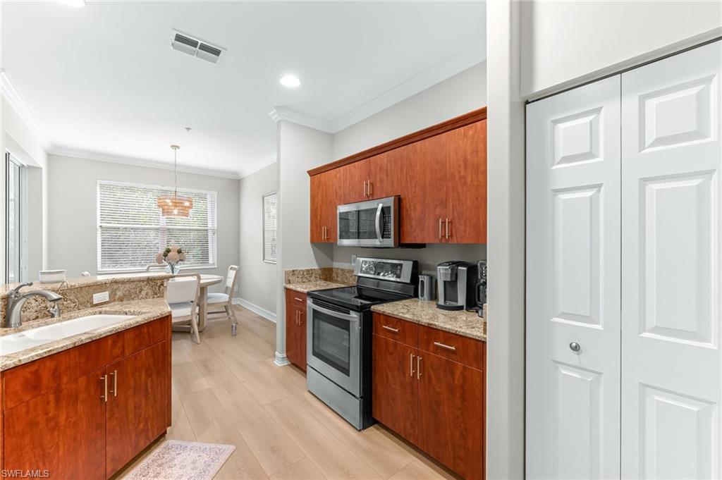 817 Carrick Bend Circle, Unit 102 Naples, FL 34110 - Photo 11 of 36 Kitchen featuring stainless steel appliances, light stone counters, crown molding, decorative light fixtures, and recessed lighting