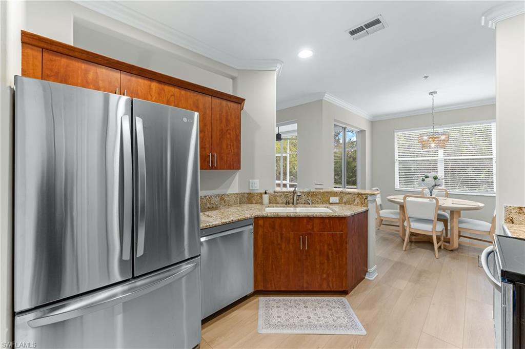817 Carrick Bend Circle, Unit 102 Naples, FL 34110 - Photo 12 of 36 Kitchen featuring appliances with stainless steel finishes, light stone countertops, crown molding, a peninsula, and brown cabinetry