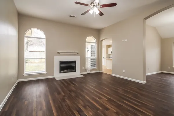 an empty room with wooden floor a ceiling fan and windows
