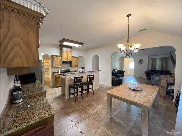 a open kitchen with granite countertop a stove a sink a dining table and chairs with wooden floor