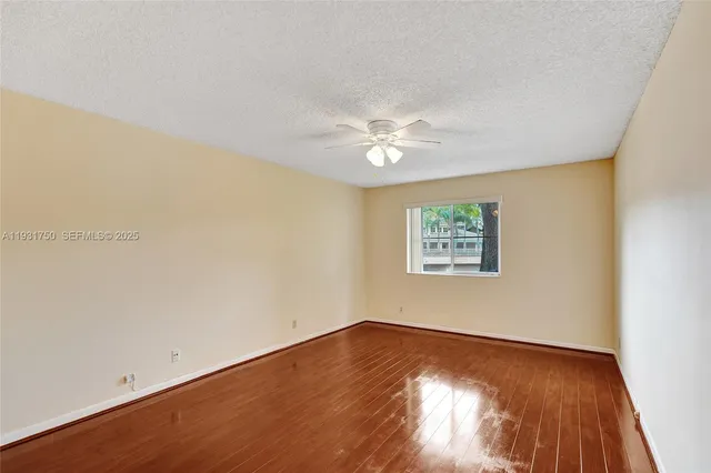 a view of an empty room with wooden floor and a ceiling fan