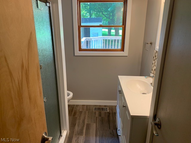 Bathroom with a shower with door, hardwood / wood-style floors, toilet, and vanity