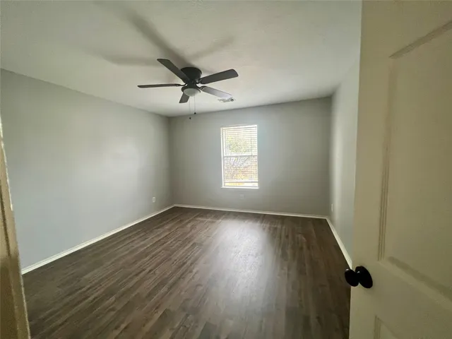 an empty room with wooden floor ceiling fan and windows