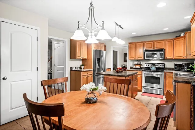 a kitchen with stainless steel appliances kitchen island granite countertop a dining table chairs and a refrigerator