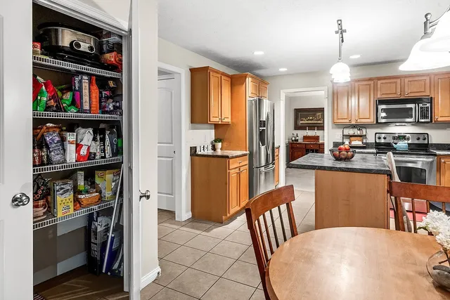 a open kitchen with stainless steel appliances granite countertop a refrigerator a stove top oven a sink and a dining table with bookshelf