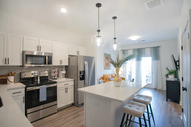 a kitchen with stainless steel appliances a stove a sink a refrigerator a center island a dining table and chairs