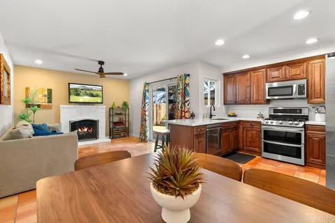 a living room with stainless steel appliances furniture a fireplace a flat screen tv and a kitchen view