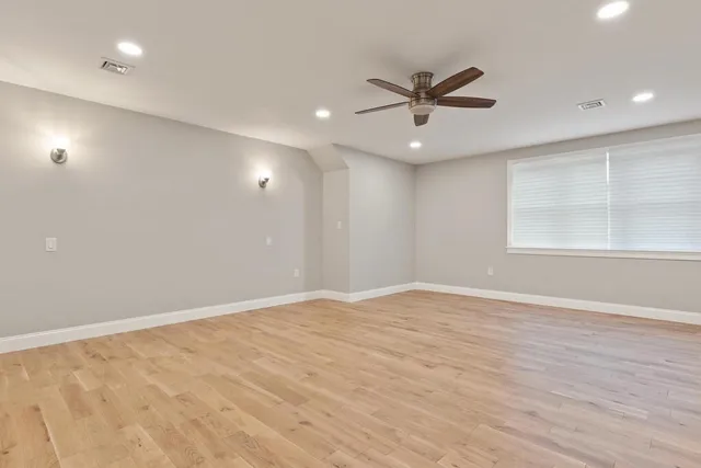 an empty room with wooden floor a ceiling fan and windows