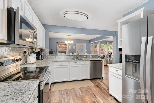 a kitchen with stainless steel appliances granite countertop a refrigerator a stove and a sink with wooden floor