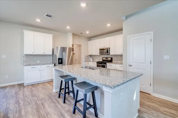 a kitchen with stainless steel appliances granite countertop a kitchen island hardwood floor sink stove and white cabinets