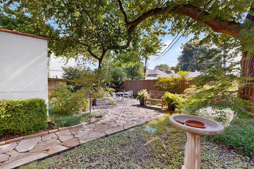 4548 Roland Avenue, Unit A Dallas, TX 75219 - Photo 28 of 31 Landscaped backyard featuring a stone patio, mature trees, and a privacy fence