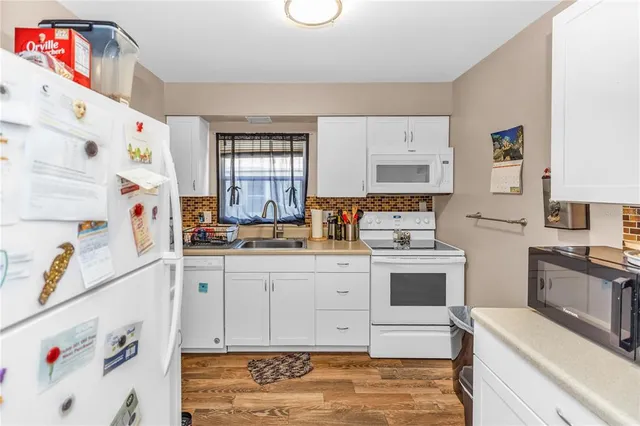 a kitchen with a white stove top oven sink and white cabinets with wooden floor
