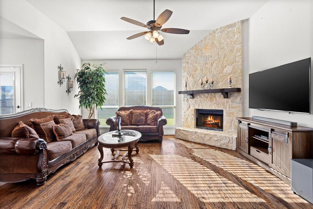 1814 Chadwick Lane Forney, TX 75126 - Photo 20 of 40 Living area featuring lofted ceiling, wood finished floors, a ceiling fan, and a stone fireplace