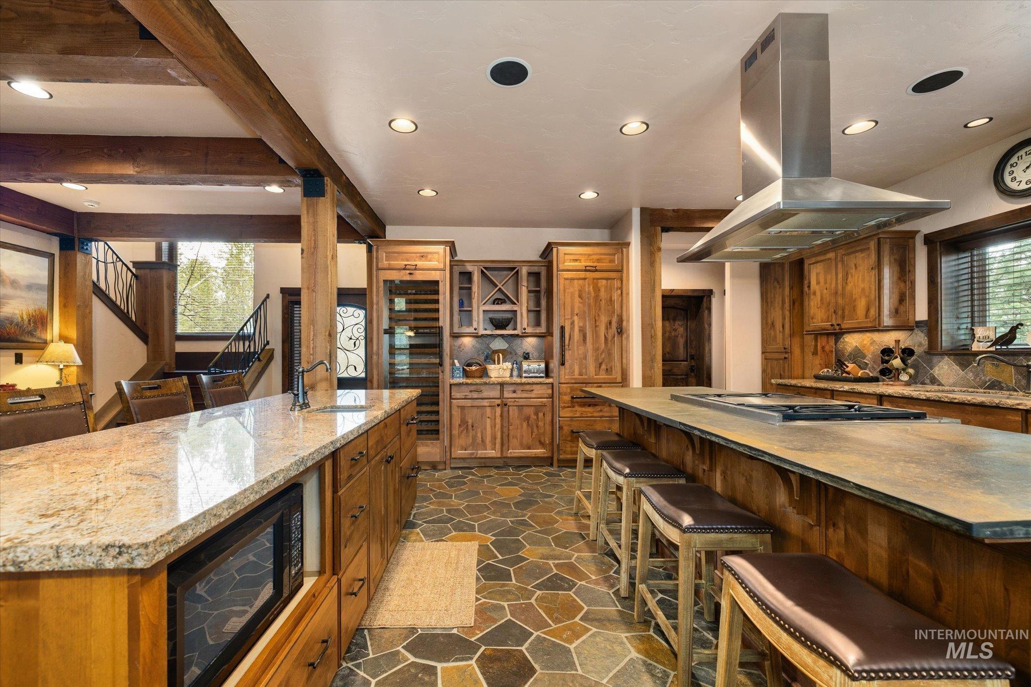 14 Pointe At Goldfork Court Donnelly, ID 83615 - Photo 12 of 49 Spacious kitchen featuring two large islands with stone countertops, a built-in cooktop with a stainless steel range hood, stone tile flooring, and exposed wood beams