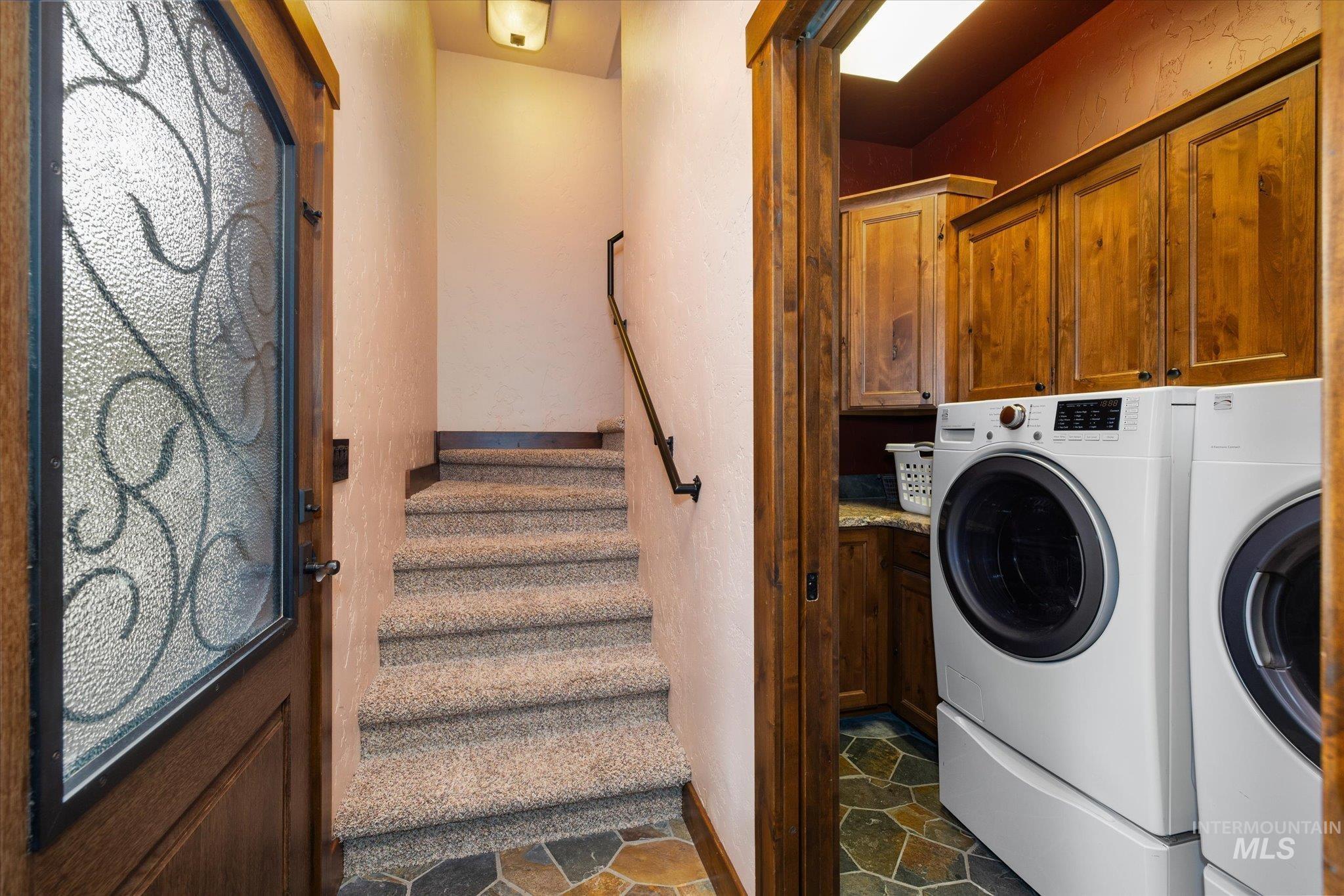 14 Pointe At Goldfork Court Donnelly, ID 83615 - Photo 30 of 49 Entryway featuring a decorative glass-paneled door with dark wood framing, carpeted stairs with a dark wood handrail, and a laundry area with wood cabinetry, a countertop, and flagstone flooring