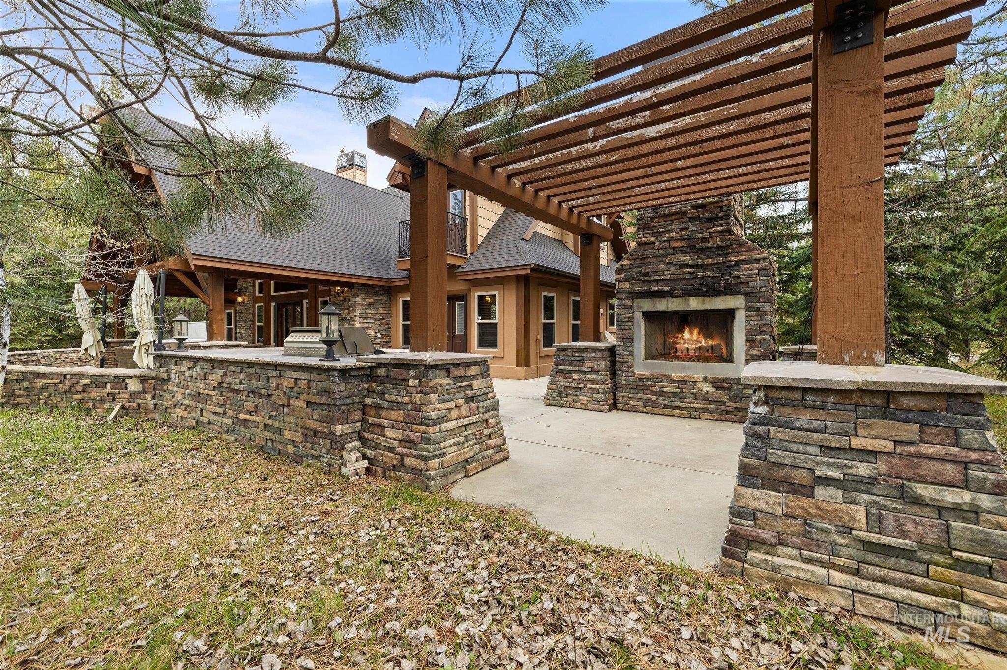 14 Pointe At Goldfork Court Donnelly, ID 83615 - Photo 39 of 49 Outdoor patio featuring a stone fireplace under a wood pergola, integrated stone planters, a paved surface, and exterior lighting fixtures