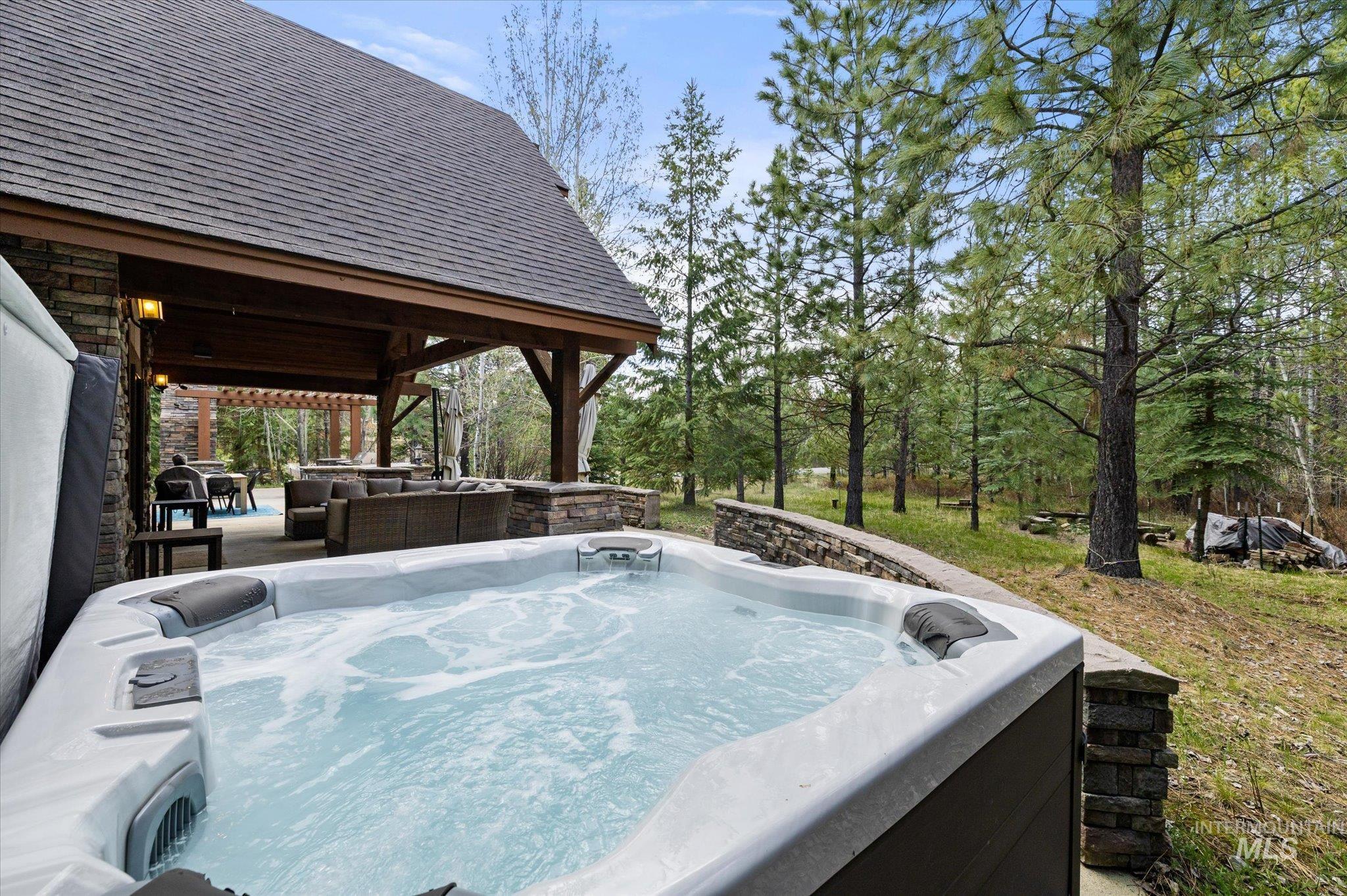 14 Pointe At Goldfork Court Donnelly, ID 83615 - Photo 40 of 49 Outdoor spa with bubbling water, stone retaining wall, and a covered patio area with exposed timber beams and an asphalt shingle roof