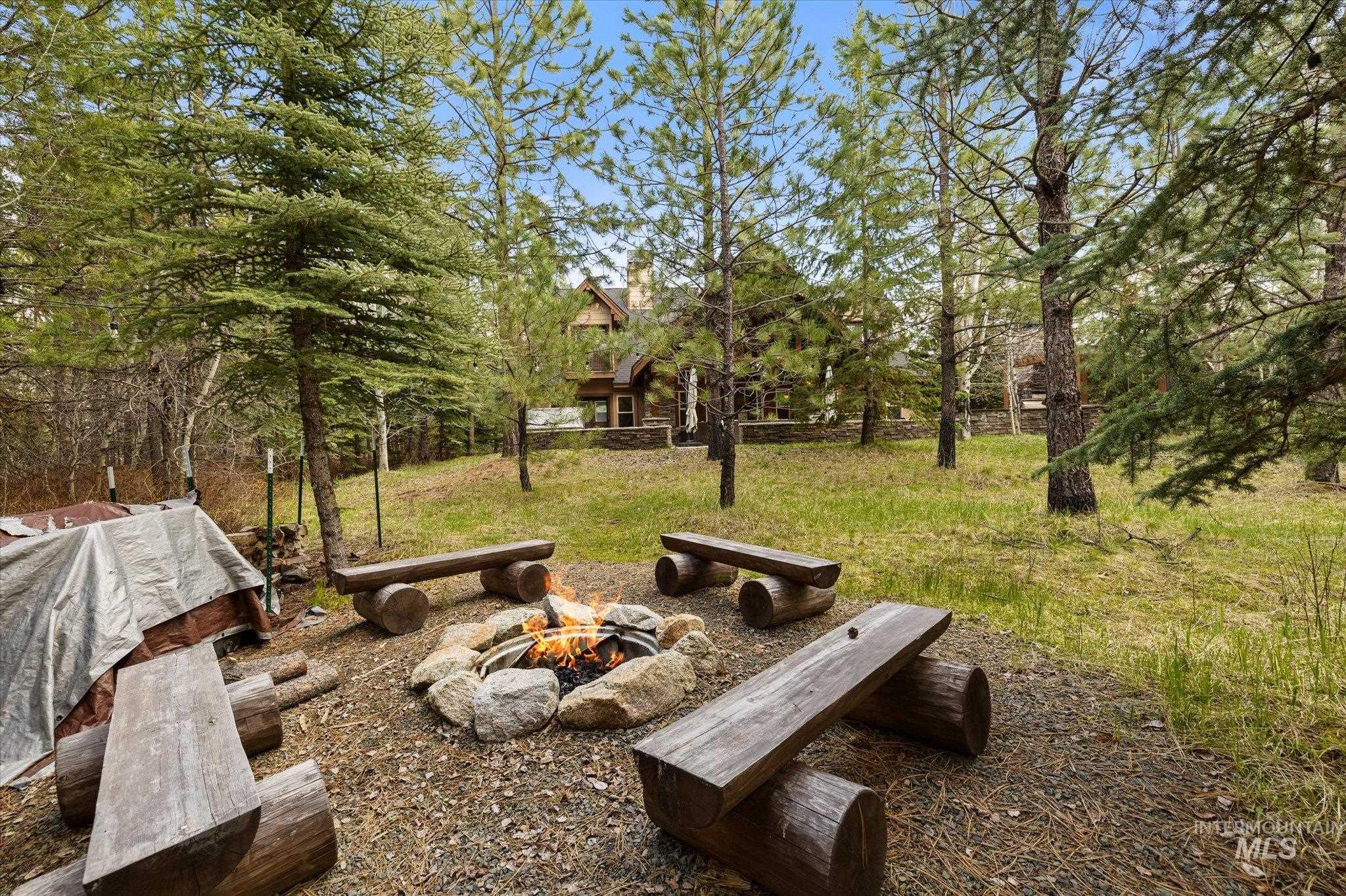 14 Pointe At Goldfork Court Donnelly, ID 83615 - Photo 41 of 49 Outdoor fire pit with natural stone surround and log benches, set within a wooded landscape featuring mature trees and a distant dwelling