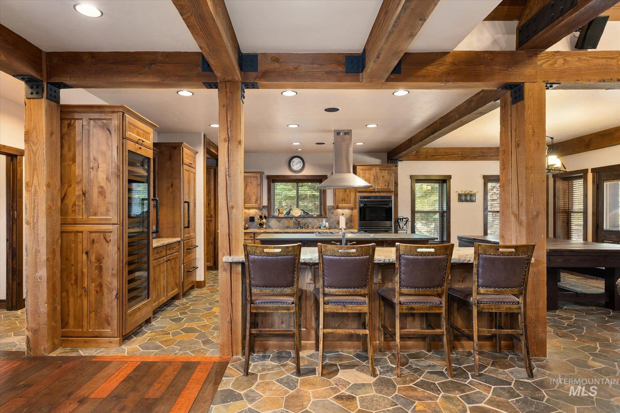 14 Pointe At Goldfork Court Donnelly, ID 83615 - Photo 9 of 49 Rustic-inspired kitchen featuring exposed wood beams, stone tile flooring, a large island with seating, integrated wine refrigeration, and stainless steel appliances