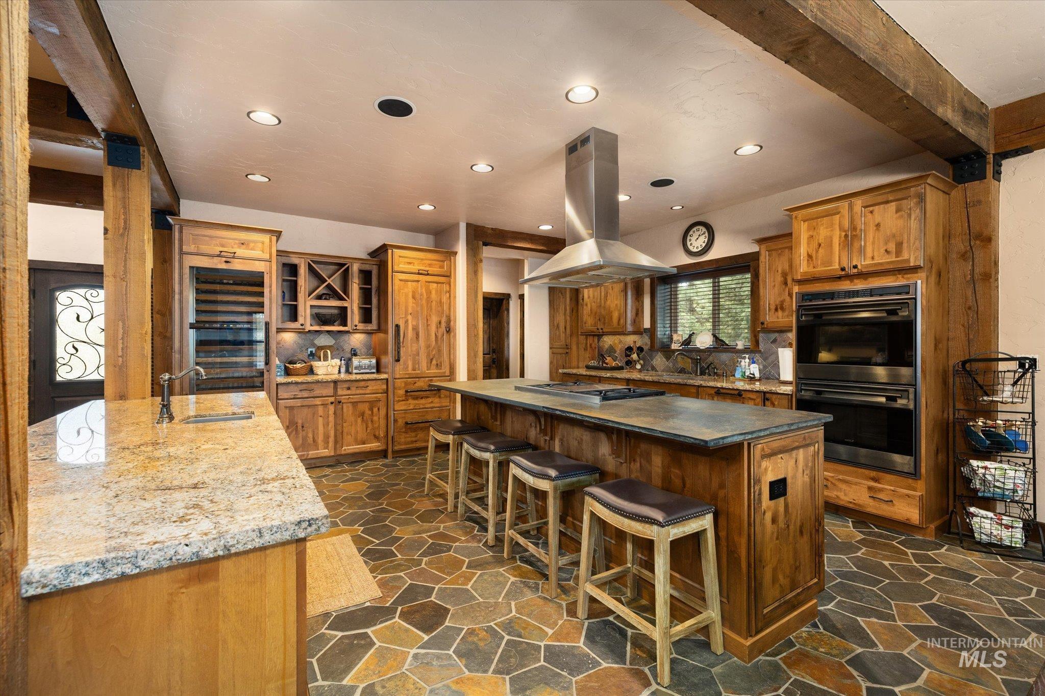14 Pointe At Goldfork Court Donnelly, ID 83615 - Photo 10 of 49 Spacious kitchen featuring natural wood cabinetry, stone tile flooring, a large central island with seating, a stainless steel range hood, and integrated double ovens
