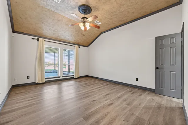 an empty room with wooden floor chandelier fan and windows