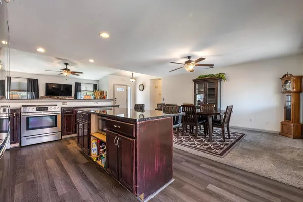 a kitchen with stainless steel appliances kitchen island granite countertop a stove top oven a sink dishwasher a dining table and chairs with wooden floor