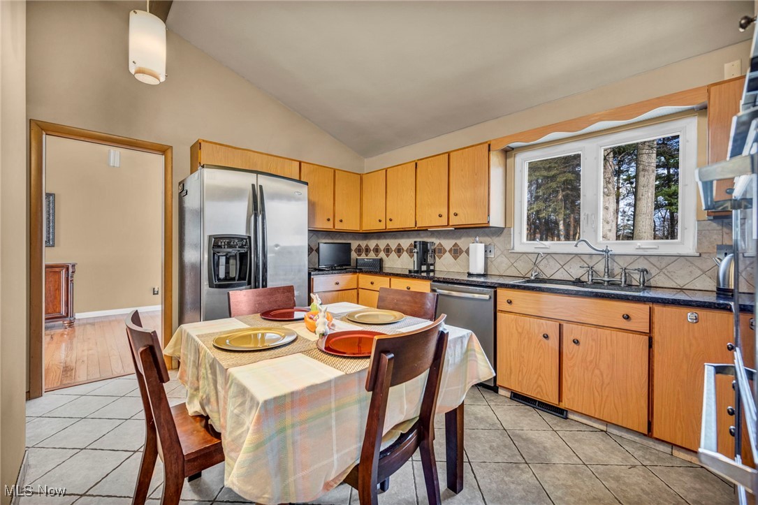Kitchen with vaulted ceiling, a sink, stainless steel appliances, light tile patterned floors, and dark countertops