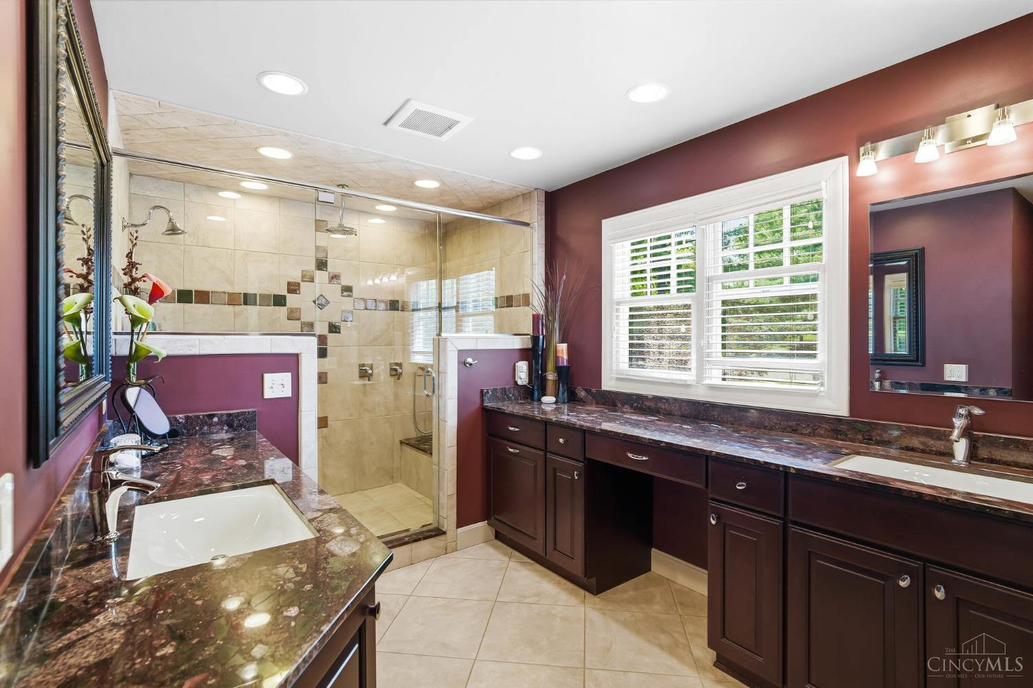 2780 Walsh Road Cincinnati, OH 45208 - Photo 29 of 68 The ensuite bath is thoughtfully designed with both comfort and functionality in mind, featuring dual vanities with rich cabinetry and expansive granite countertops that provide ample space for everyday routines. Warm, sophisticated finishes are complemented by abundant natural light, creating a bright yet inviting atmosphere. The oversized walk-in shower serves as a true focal point, showcasing full tile surround, decorative inlay accents, multiple shower heads, and a built-in bench for added convenience. A private water closet enhances the layout, offering both privacy and practicality, while generous storage throughout completes this well-appointed primary bath.