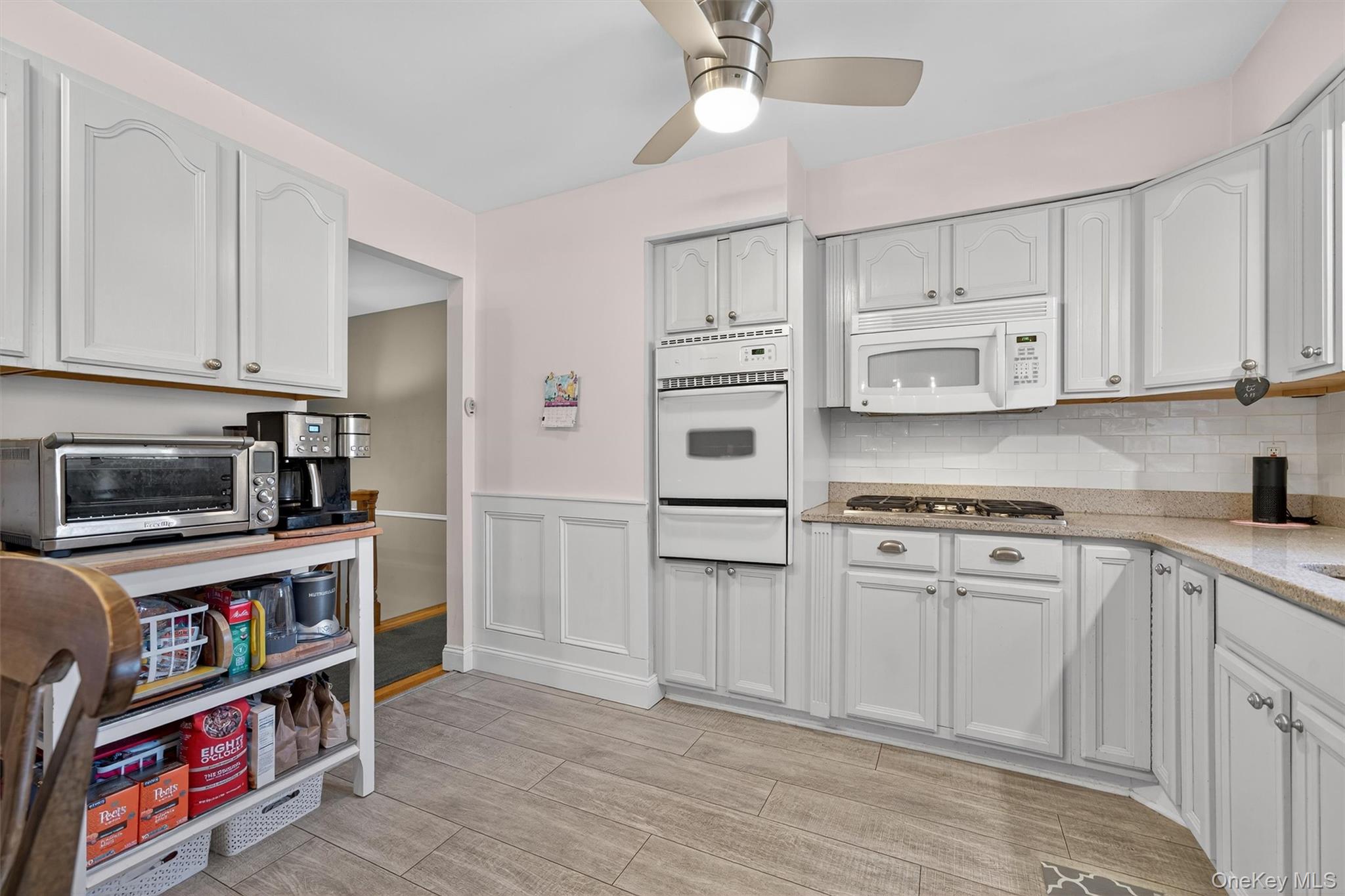 76 Pine Hill Road Highland Mills, NY 10930 - Photo 14 of 41 Kitchen featuring light stone counters, a wainscoted wall, white appliances, white cabinetry, and wood finish floors