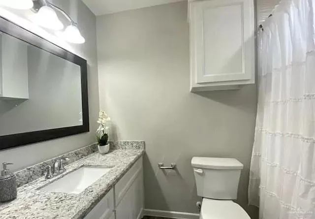 a bathroom with a granite countertop sink toilet and mirror
