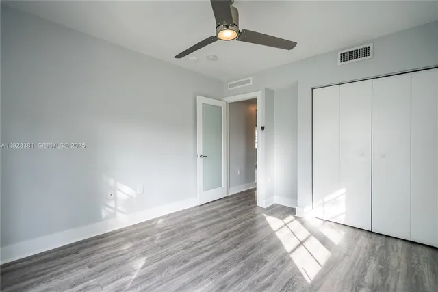 a view of an empty room with wooden floor and a ceiling fan