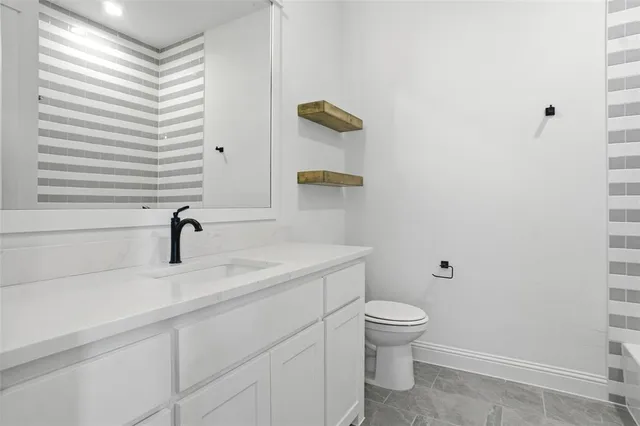 a bathroom with a granite countertop toilet a sink and a mirror