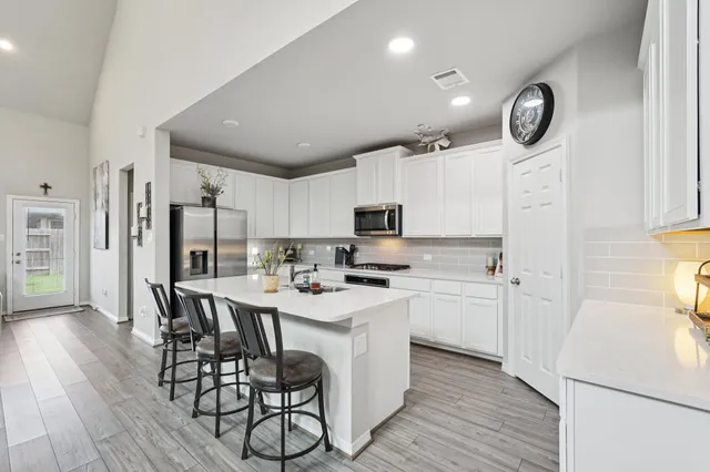 a kitchen with stainless steel appliances a stove a sink dishwasher a refrigerator with white cabinets and wooden floor