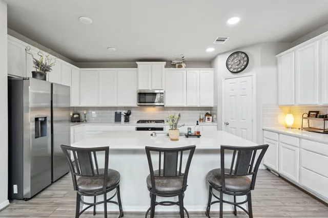 a kitchen with stainless steel appliances a table chairs refrigerator sink and cabinets