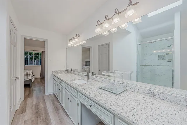 a spacious bathroom with a granite countertop double vanity sink a mirror and a shower