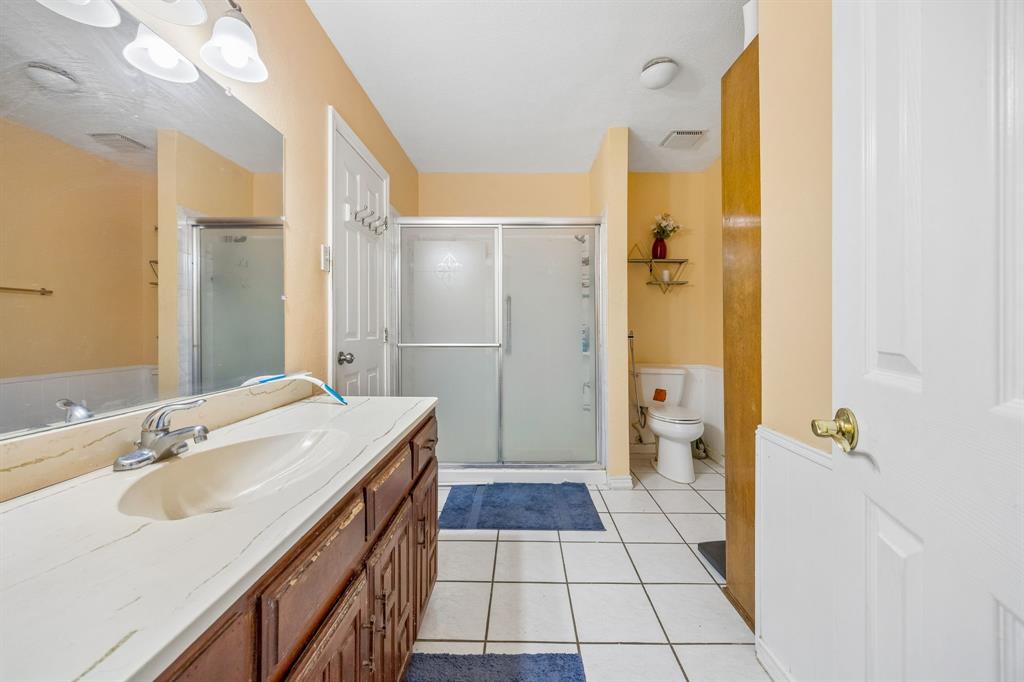 1701 East Spring Valley Road Richardson, TX 75081 - Photo 25 of 28 Bathroom featuring a wood-finish vanity with an integrated sink, shower with a sliding glass door, and tile flooring