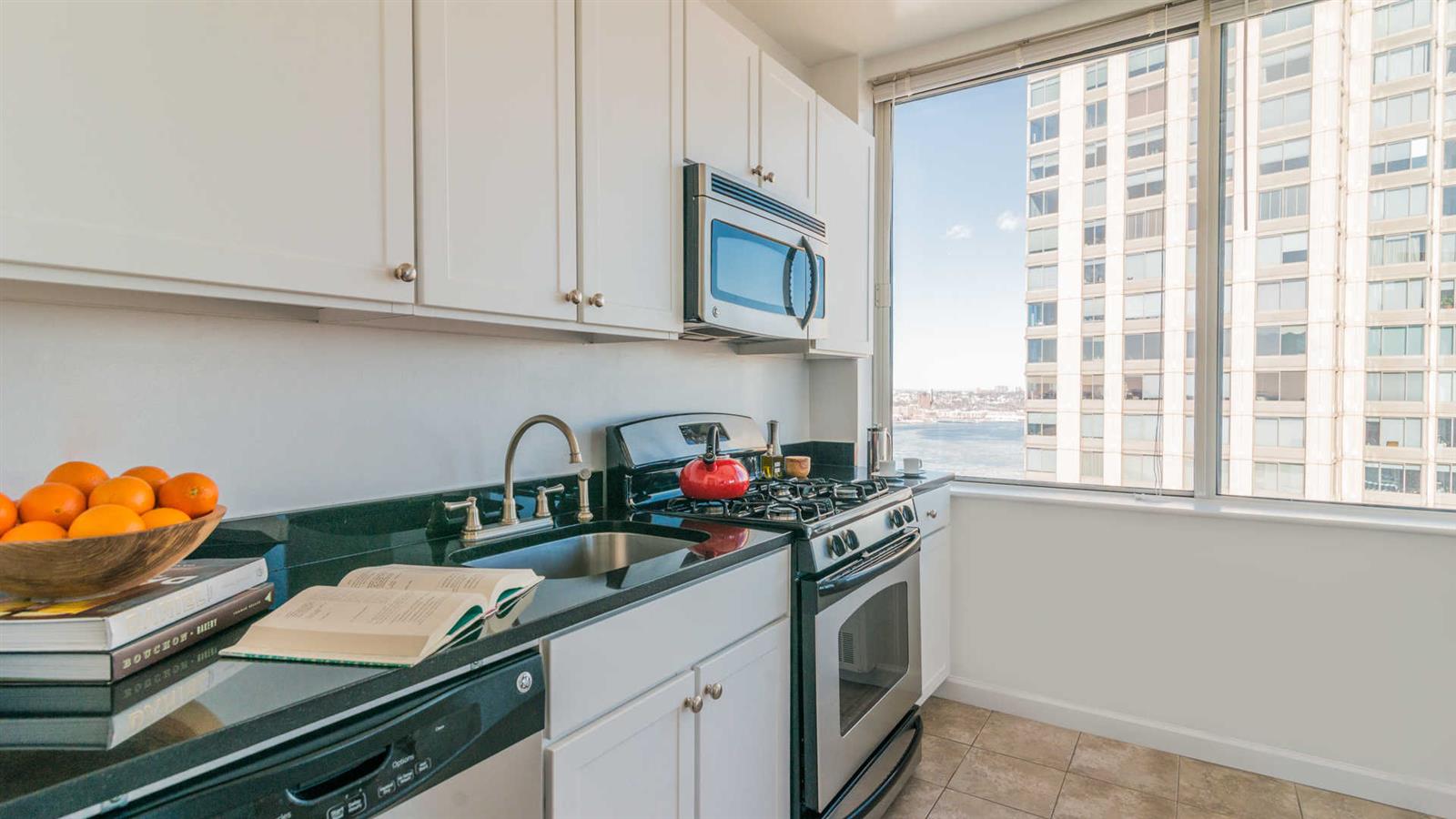 180 Riverside Boulevard, Unit 9M Manhattan, NY 10069 - Photo 5 of 10 a kitchen with stainless steel appliances granite countertop a sink dishwasher and cabinets with wooden floor
