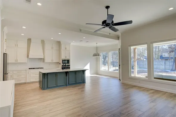 a view of an empty room with wooden floor and a kitchen