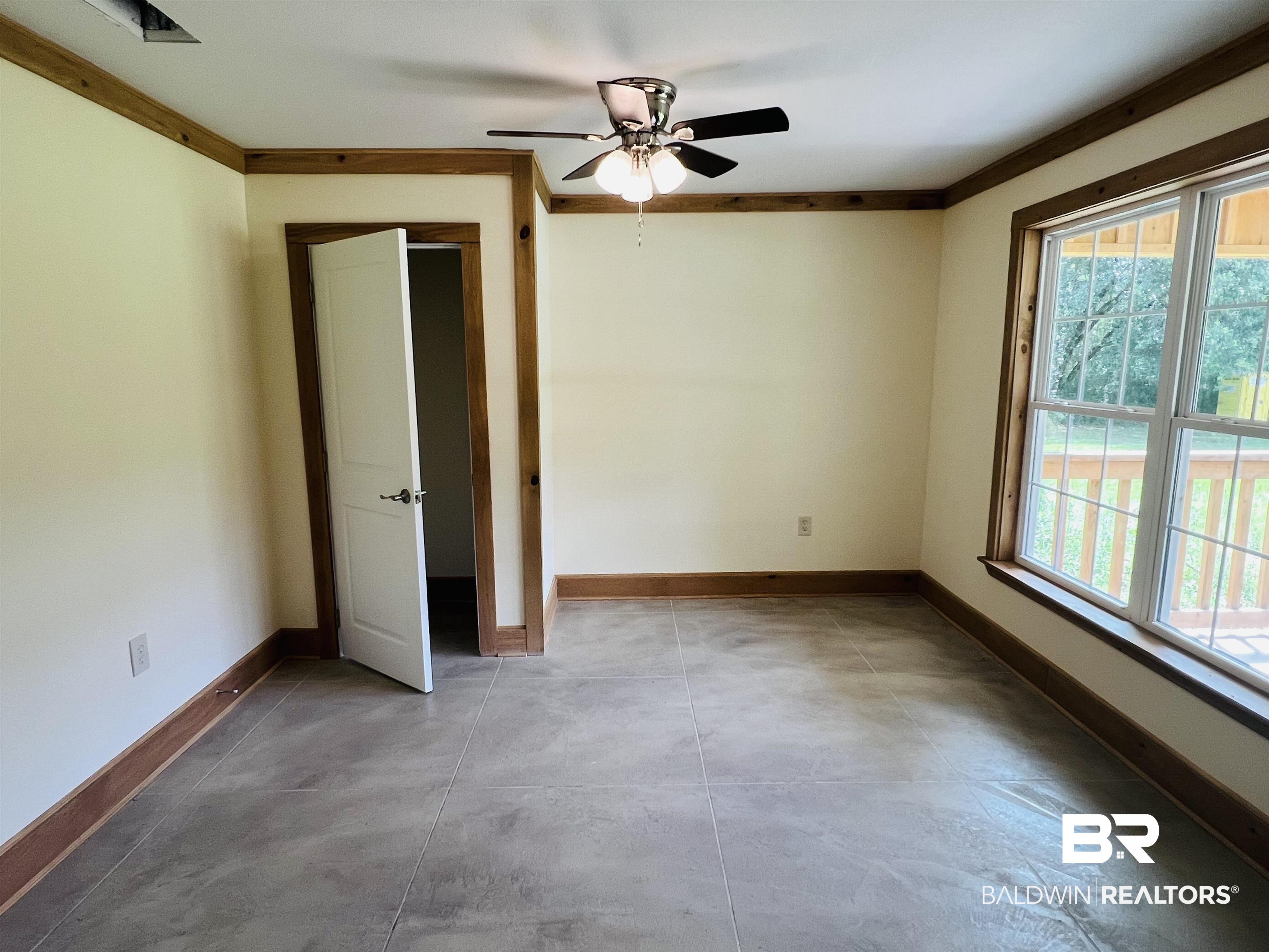 29685 Gardner Road Elberta, AL 36530 - Photo 8 of 16 Spacious room featuring wood-finish trim and baseboards, a ceiling fan with light fixture, large window, and tile flooring