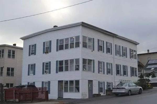 a front view of a building with lot of cars and trees