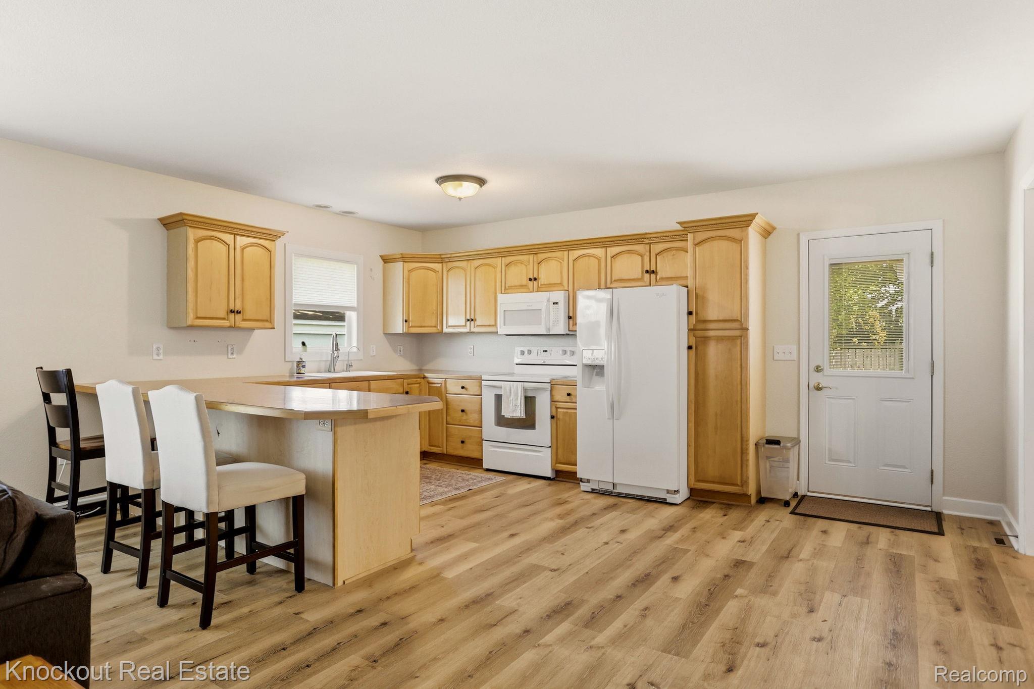 9941 Lange Road Birch Run, MI 48415 - Photo 11 of 42 Open-concept kitchen featuring wood-finish flooring, light wood cabinetry, white appliances, and a breakfast bar