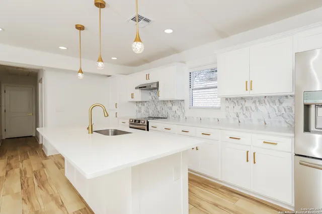 a kitchen with a sink a stove a refrigerator and white cabinets with wooden floor