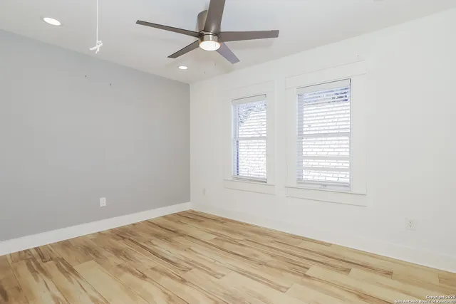 an empty room with wooden floor ceiling fan and windows