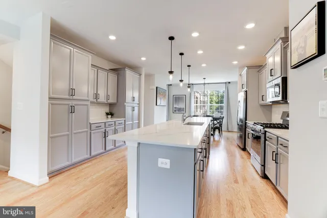 a kitchen with stainless steel appliances kitchen island granite countertop a stove top oven a sink a refrigerator and white cabinets with wooden floor