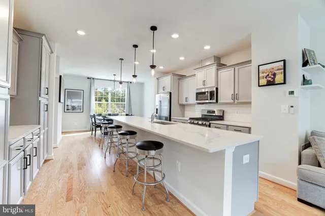 a kitchen with stainless steel appliances a stove a sink a refrigerator a couch and white cabinets with wooden floor