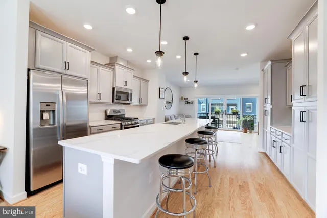 a kitchen with stainless steel appliances kitchen island granite countertop a refrigerator a stove oven a sink with island and chairs with wooden floor